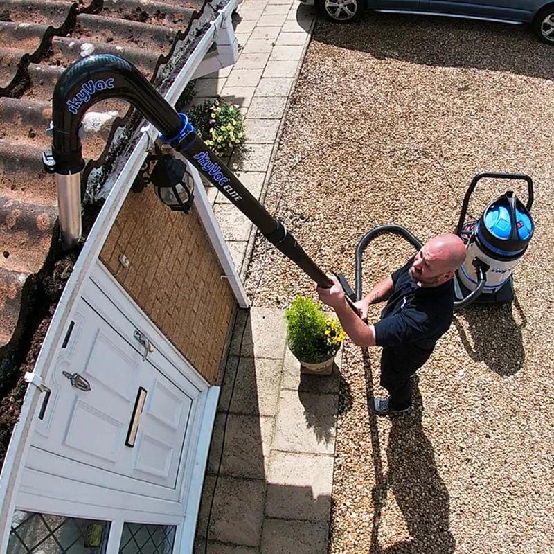 Operative clearing a house gutter from ground level with a vacuum pole system